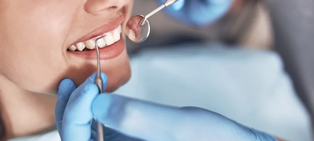 Dentysta bada okolice szyjek zębowych pacjentki za pomocą lusterka stomatologicznego.