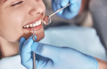 Dentysta bada okolice szyjek zębowych pacjentki za pomocą lusterka stomatologicznego.