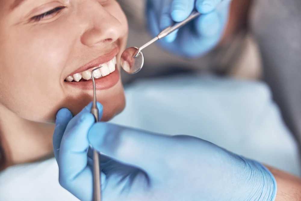 Dentysta bada okolice szyjek zębowych pacjentki za pomocą lusterka stomatologicznego.